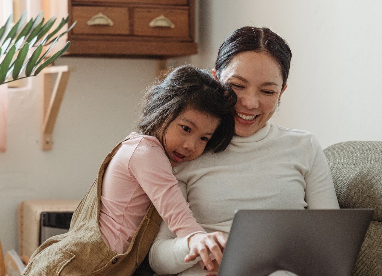 An Asian mother and her daughter look at a laptop together.