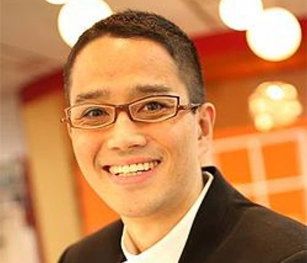 A picture of Satoshi Tajiri, a Japanese man with a buzzcut wearing spectacles.
