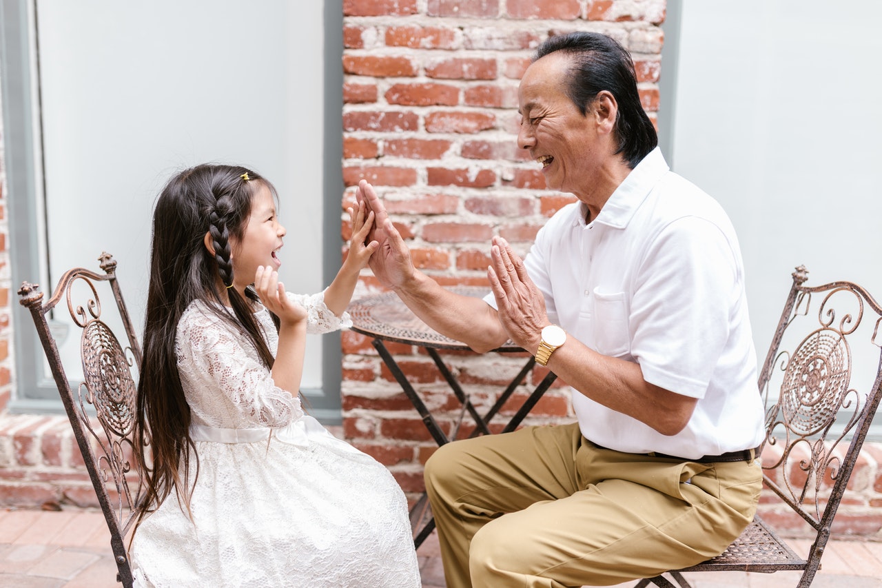 A young girl plays a hand clapping game with an older man