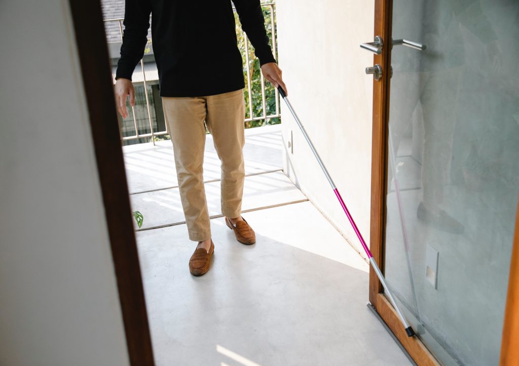 A blind person stands in an open doorway with their cane