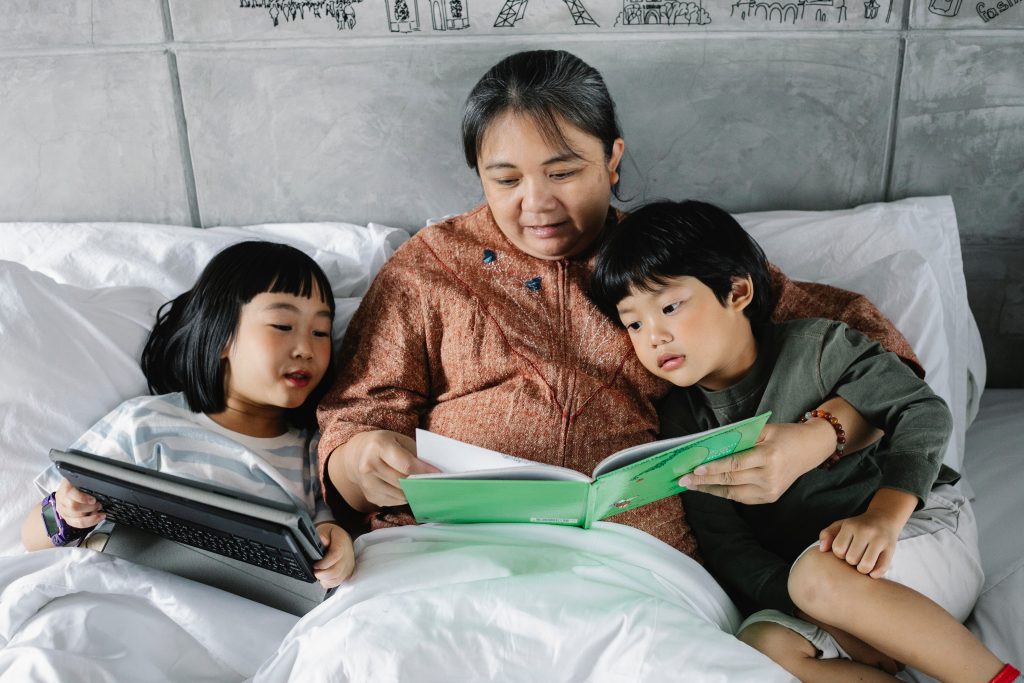 An old woman and two children reading in bed