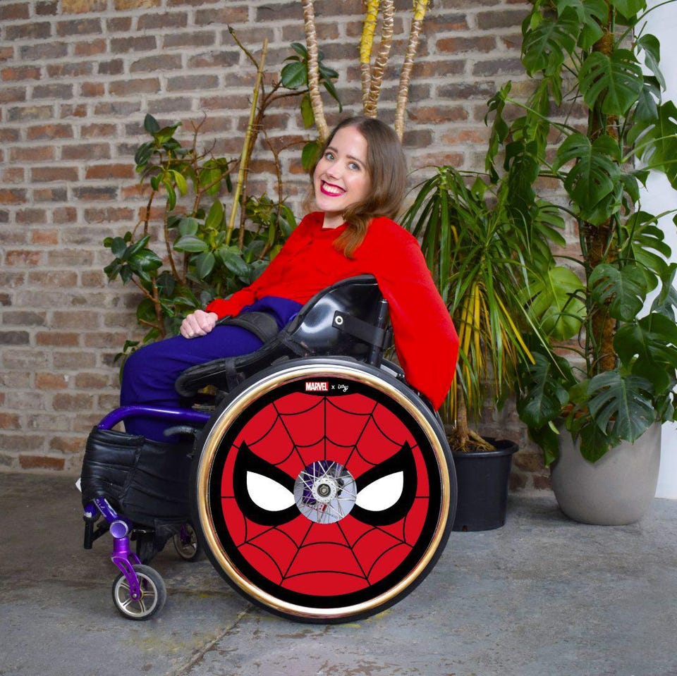 A woman with bright red lipstick seated in a wheelchair with Spider-Man wheel covers