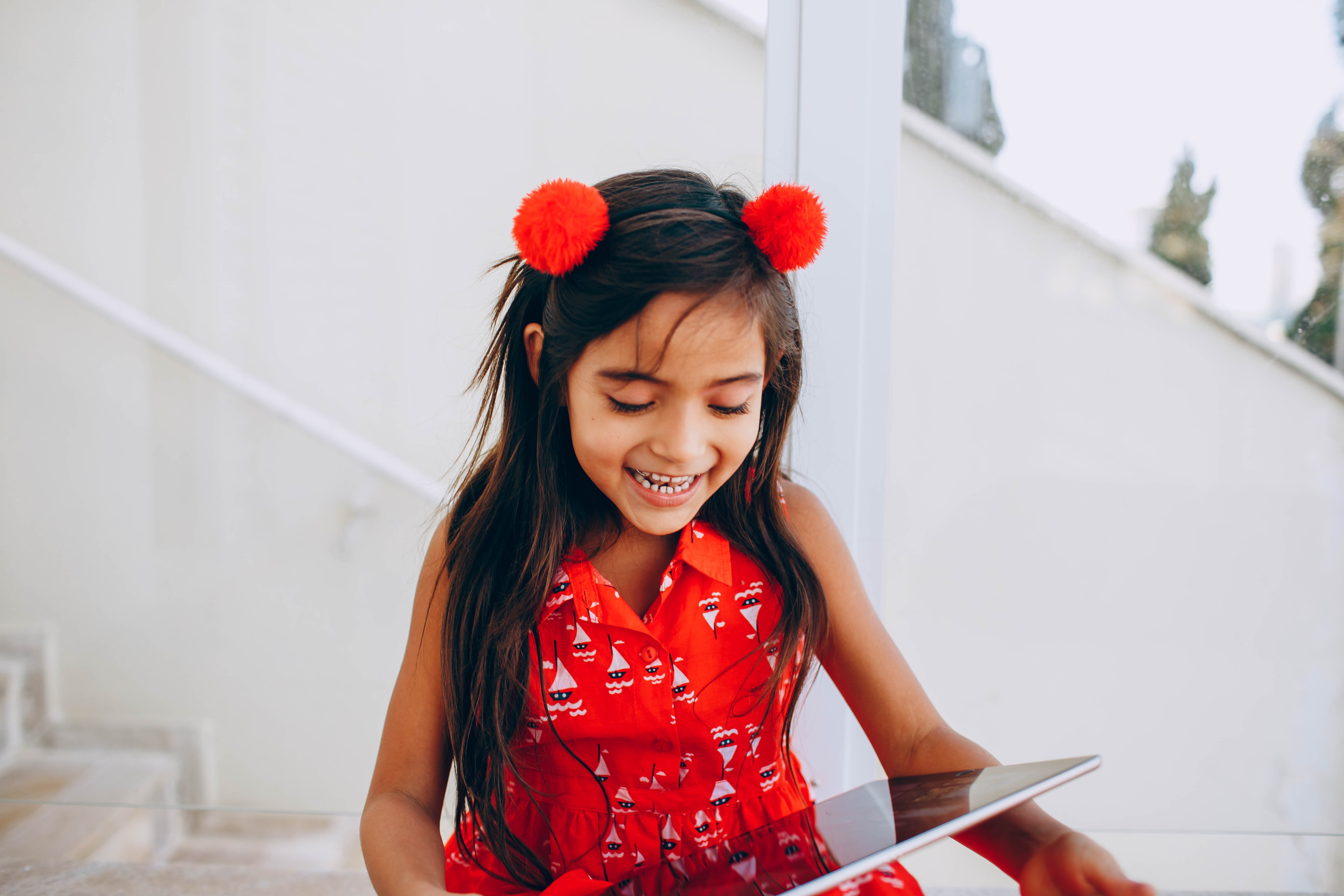A girl dressed in red laughs at a tablet