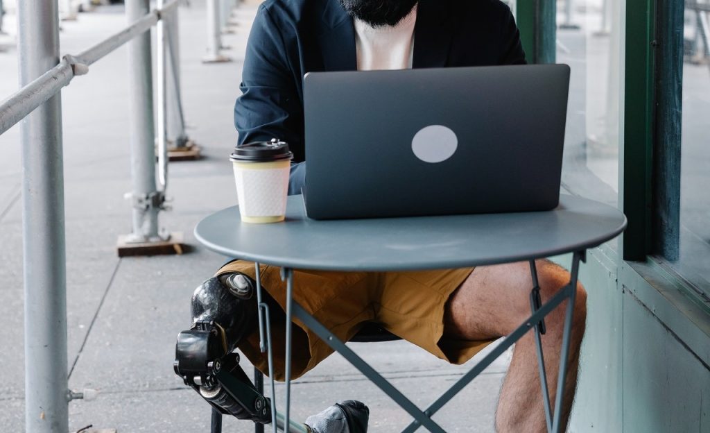 An amputee works on their laptop at a small table