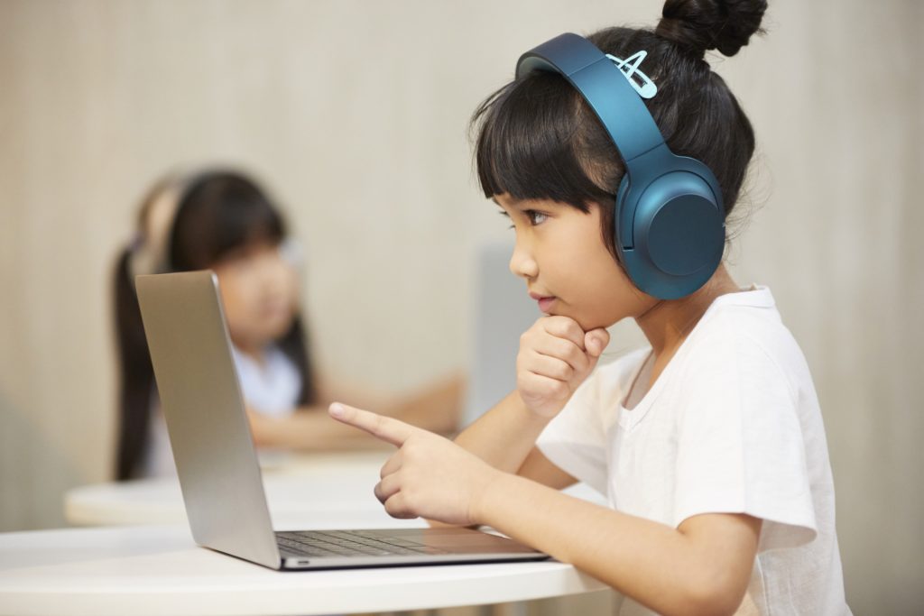 An East Asian child points at a laptop screen while making a thinking face.