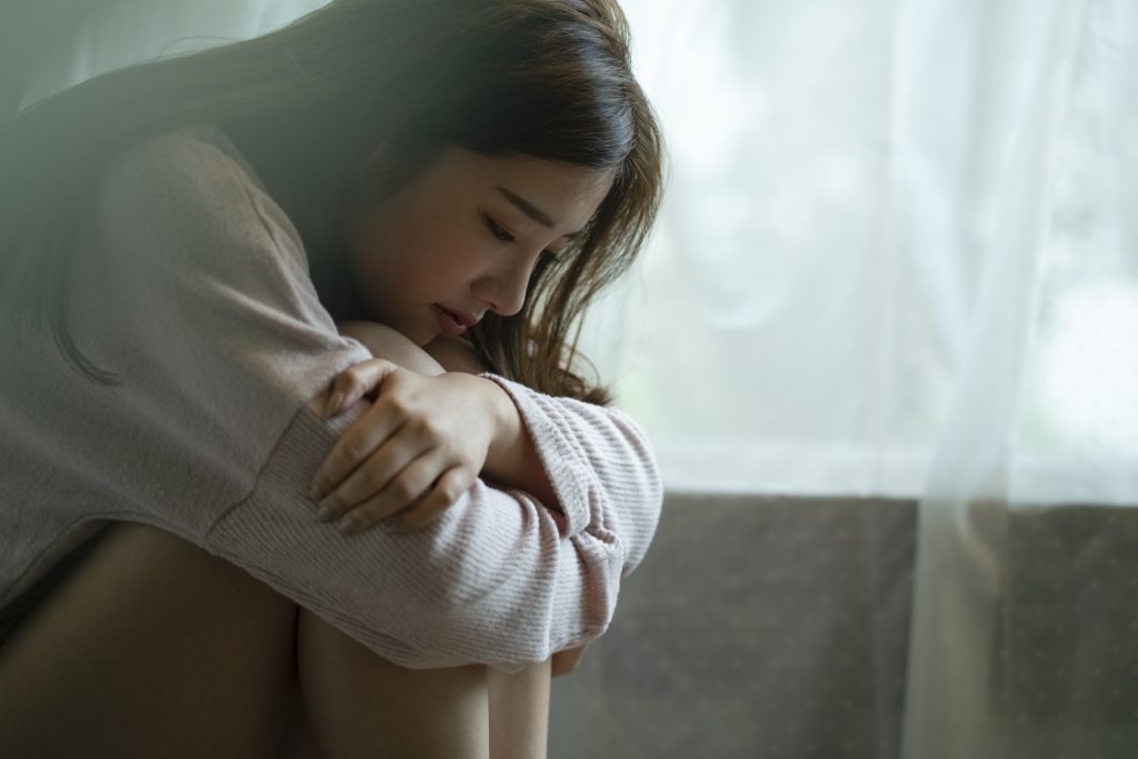 A young woman sitting by a window, looking sad and tired.