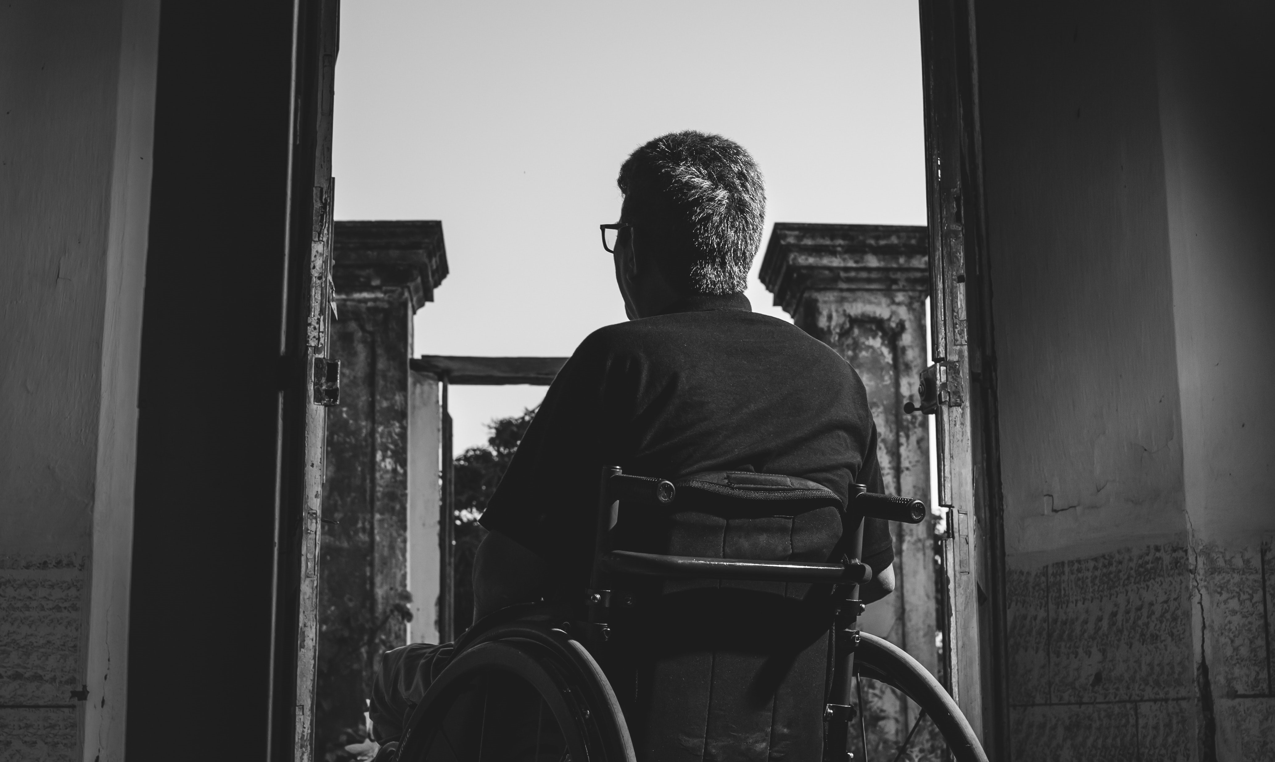 A black and white photo of a man in a wheelchair, framed by a large doorway